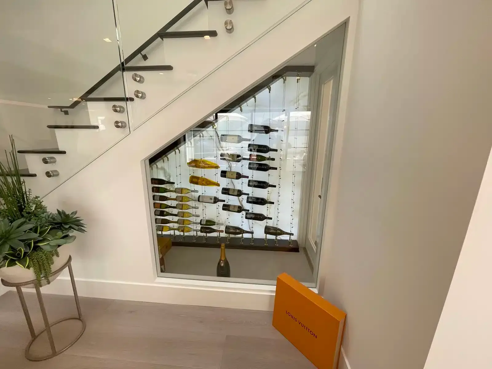 Under-stairs wine cellar with bottles behind a glass panel in a home interior