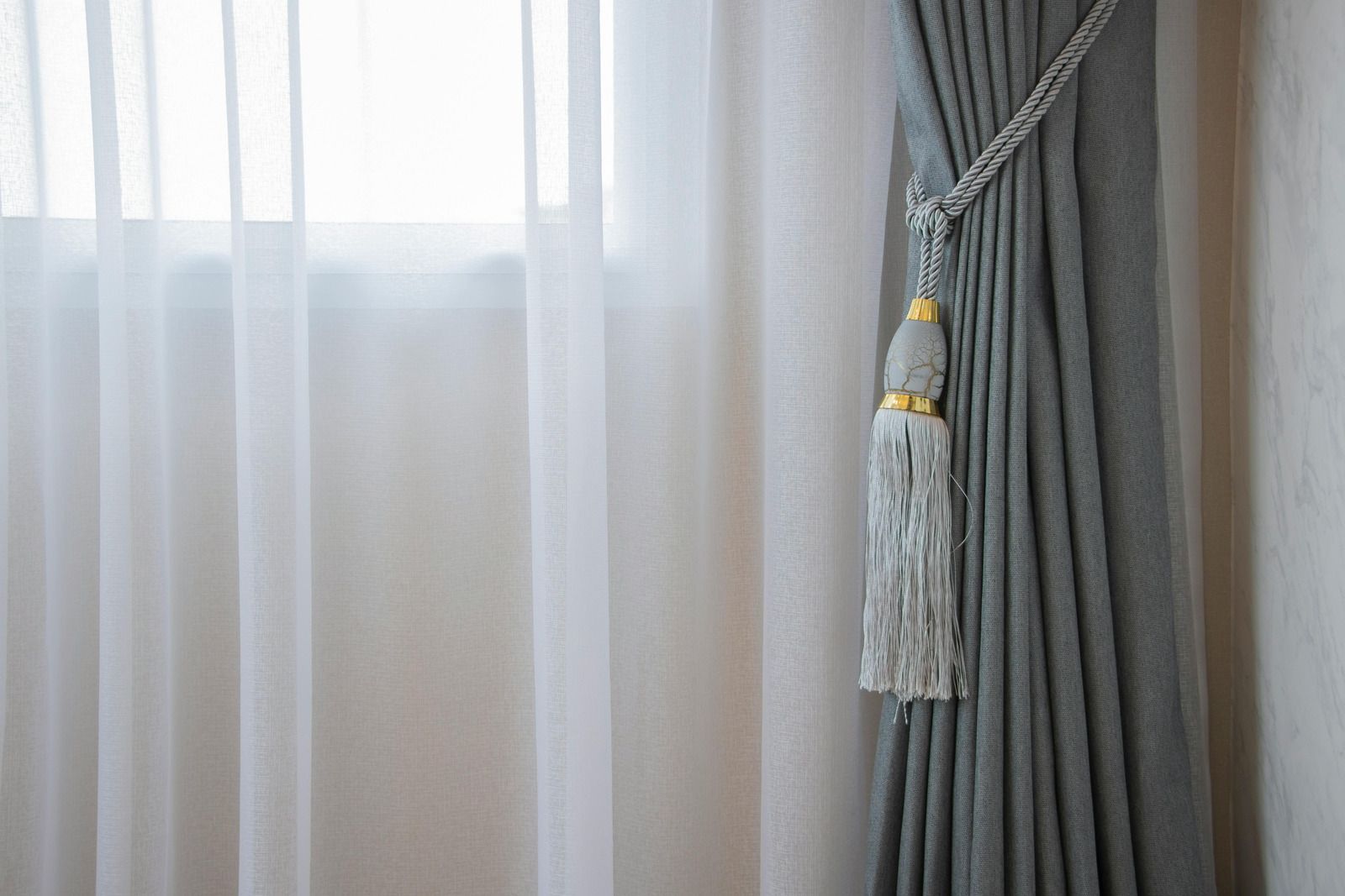 A close up of a grey curtain with a tassel attached to it.