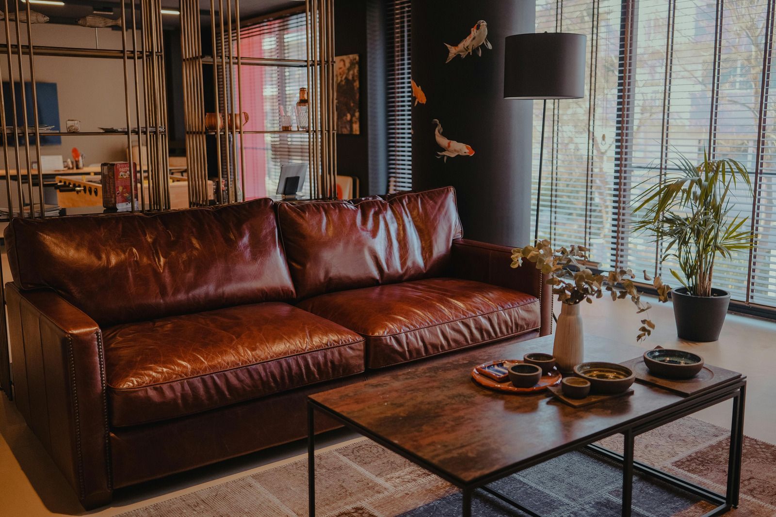 Brown leather couch in a room with dark walls, a window, and a small coffee table.