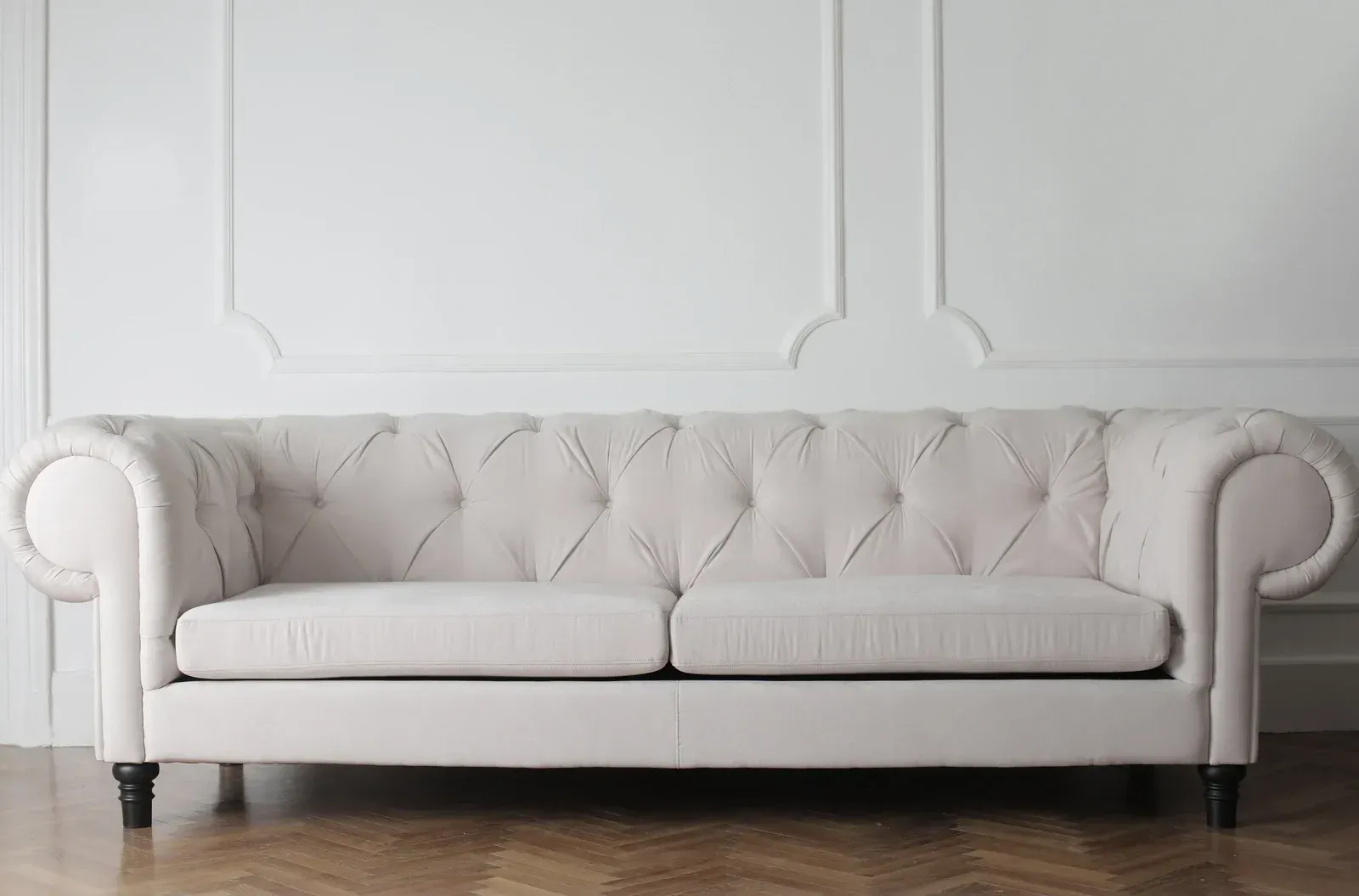 Cream-colored tufted sofa against a white wall with molding, set on a wood floor.