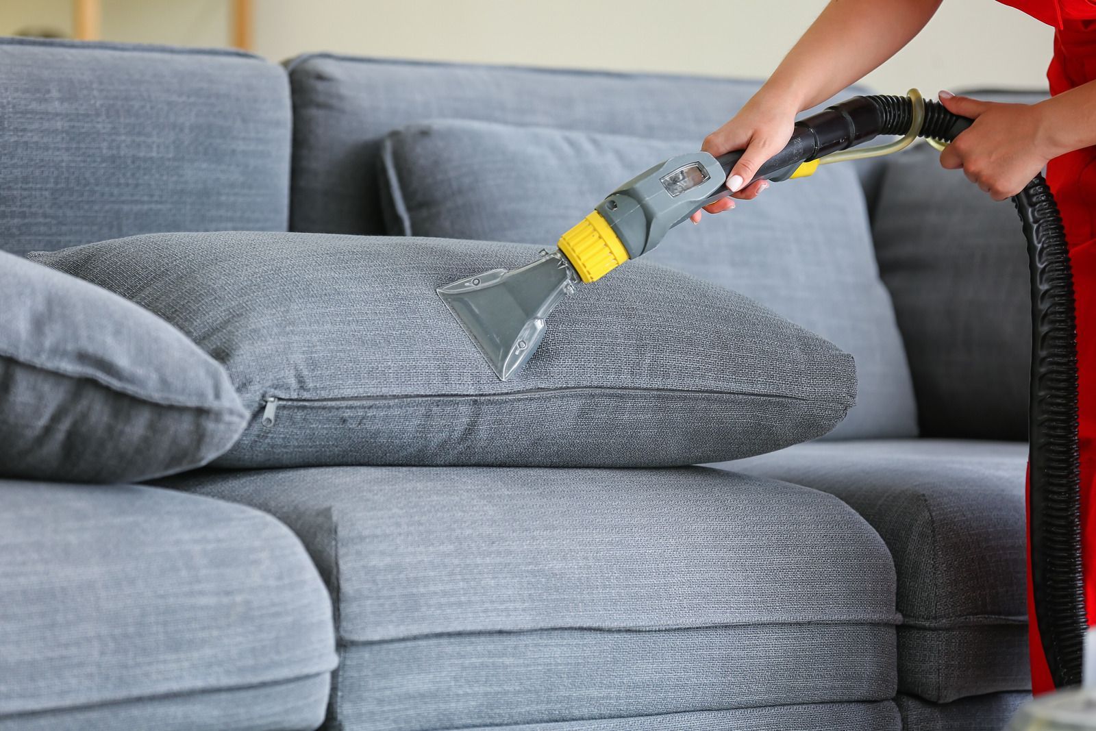 A person is cleaning a couch with a vacuum cleaner.