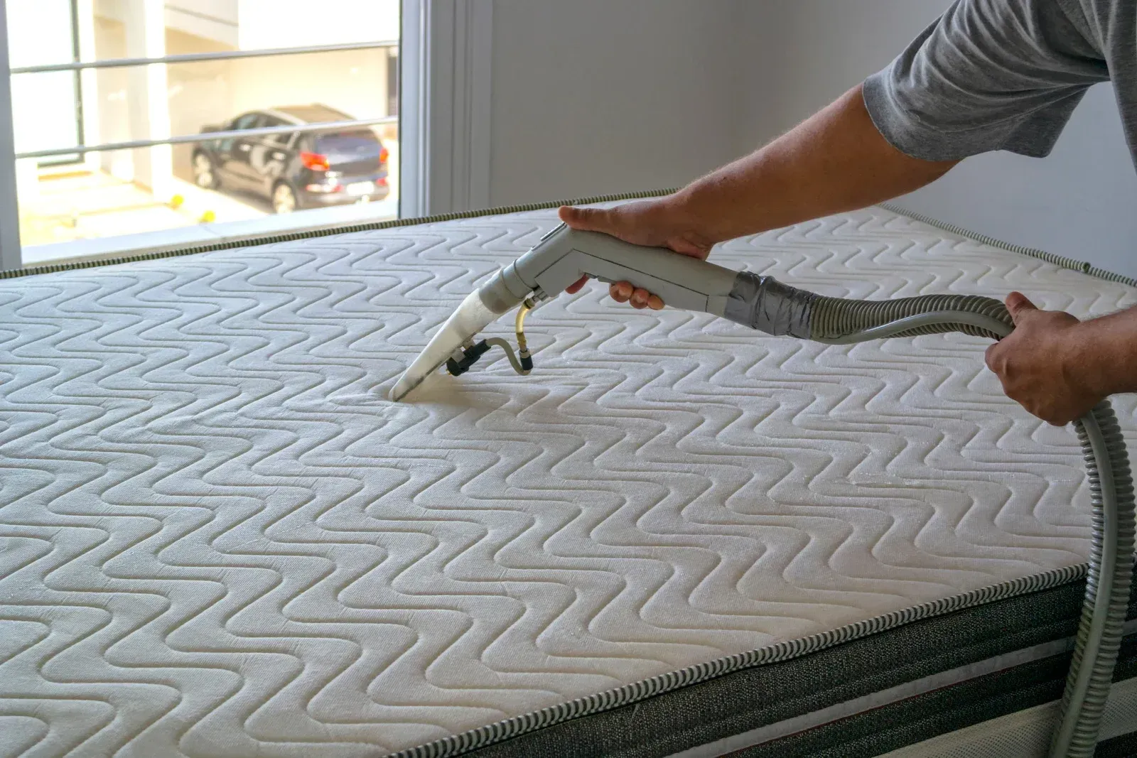 A person is cleaning a mattress with a vacuum cleaner.