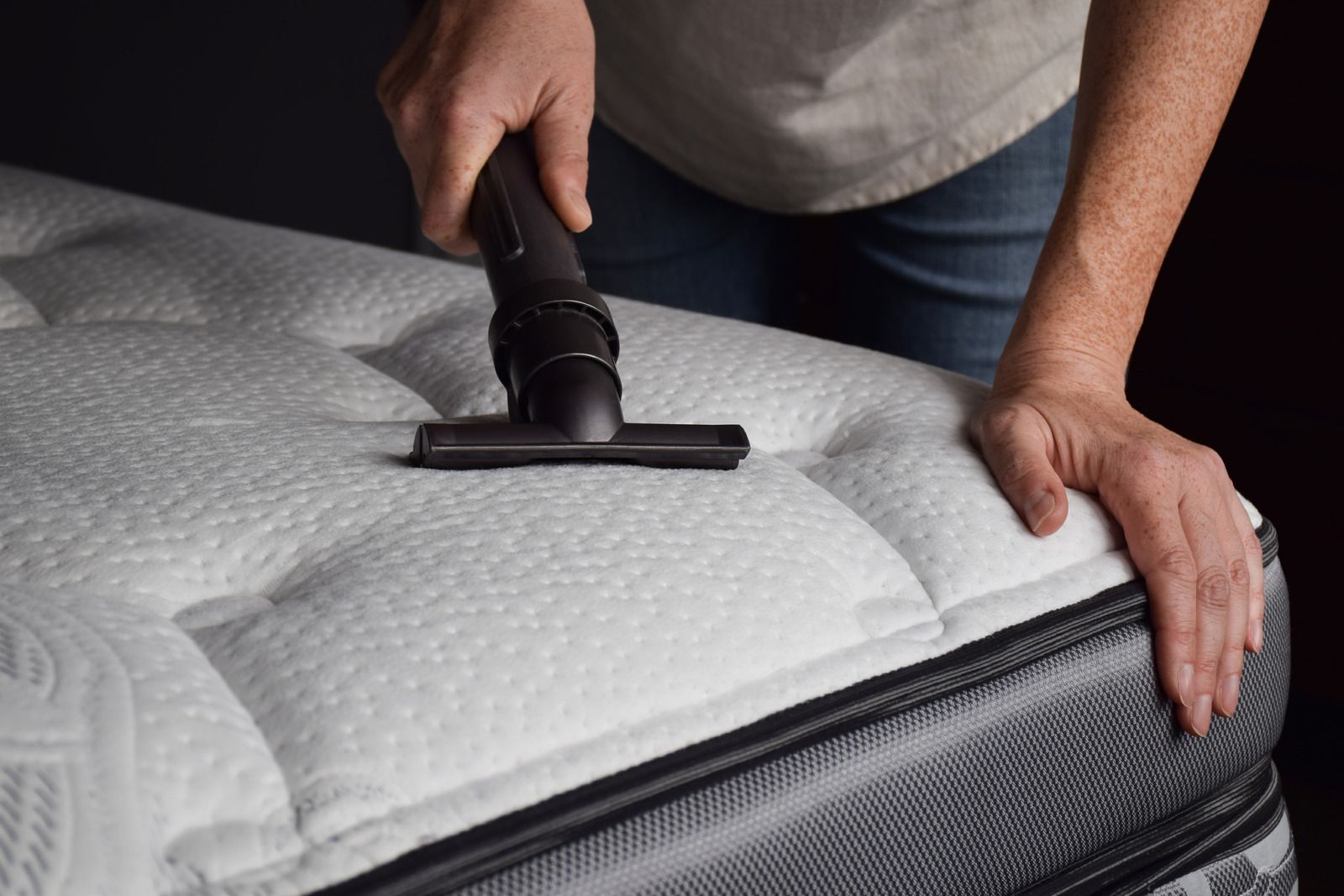 A person is vacuuming a mattress with a vacuum cleaner.