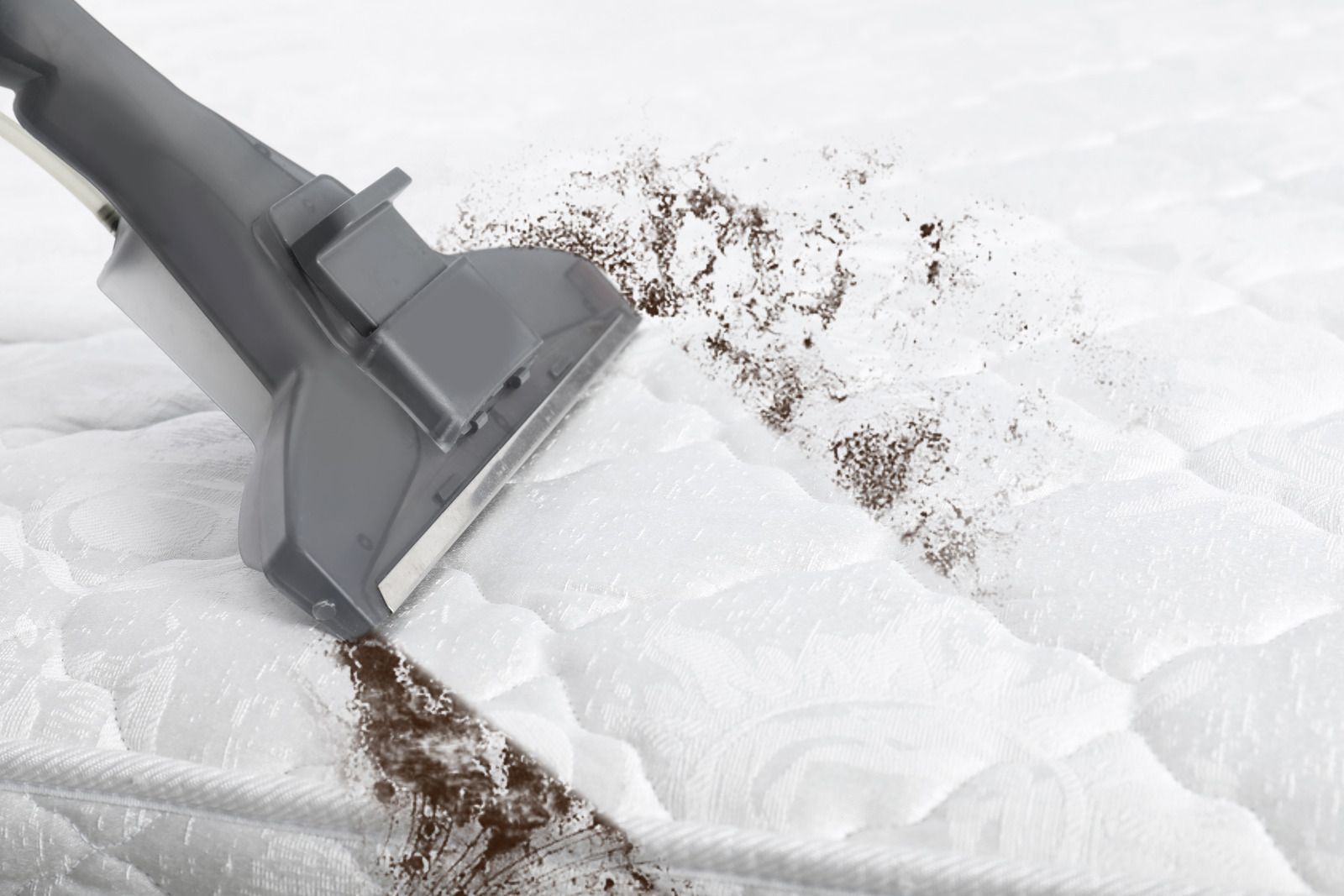 A vacuum cleaner is cleaning a mattress with dust on it.