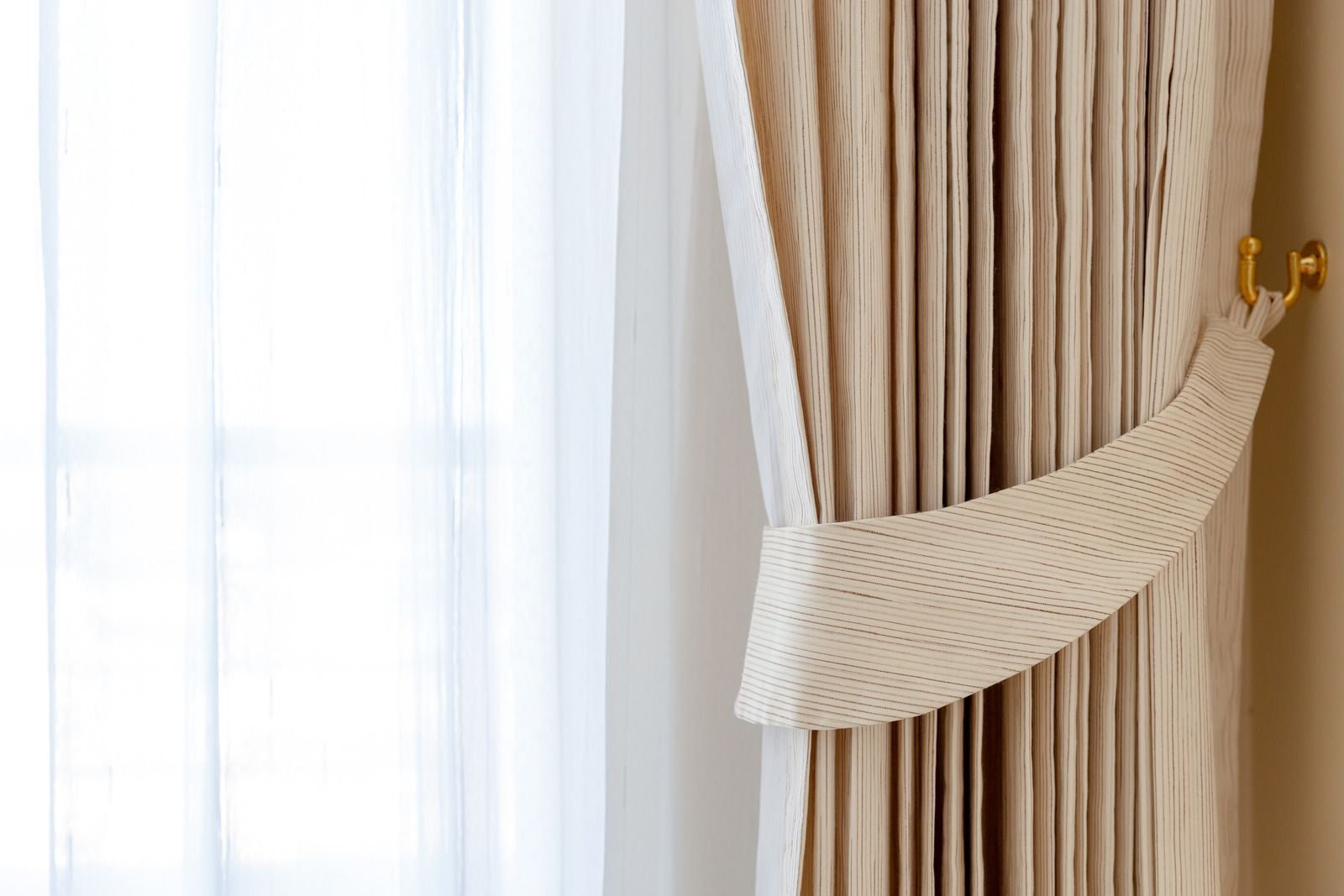 A woman is cleaning curtains with a vacuum cleaner.