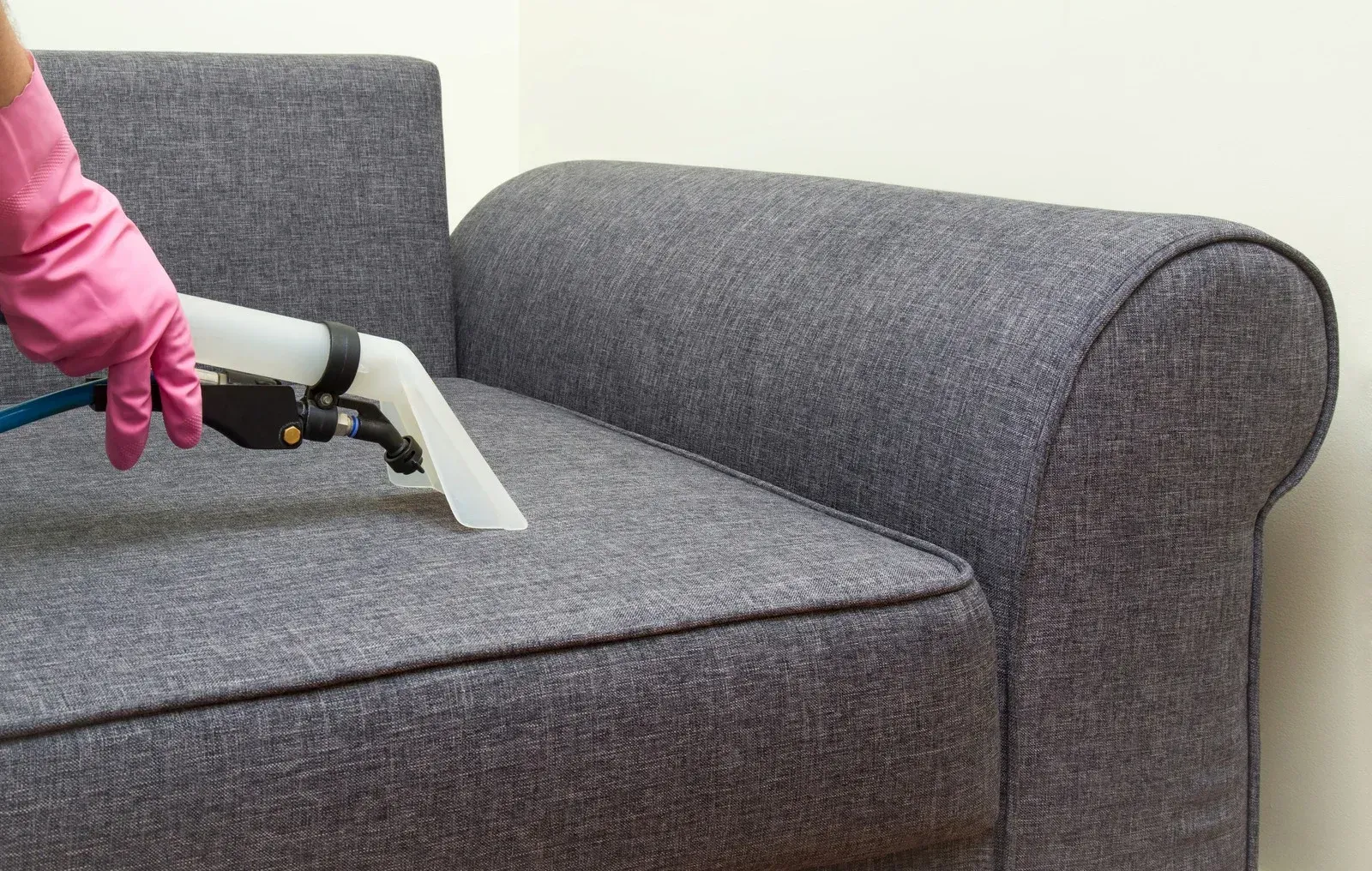 A person is cleaning a couch with a vacuum cleaner.