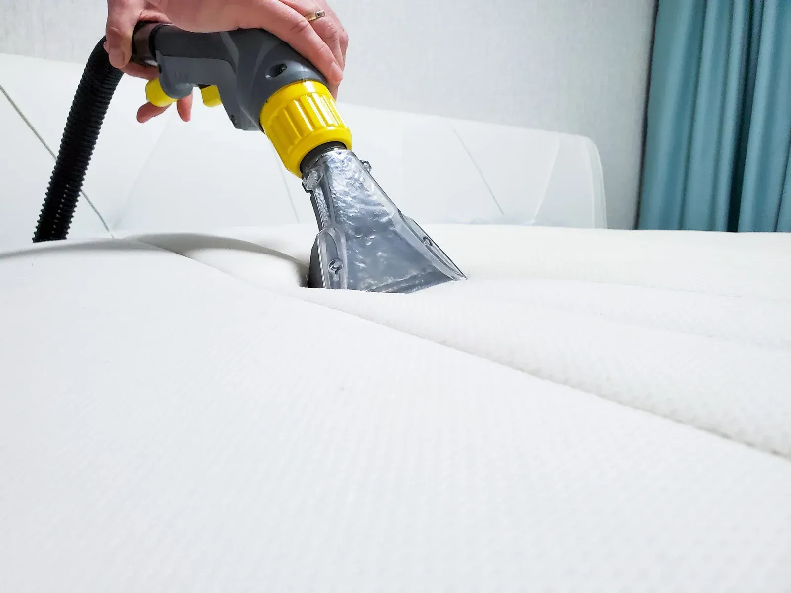 Person using a cleaning tool on a white mattress, removing dirt.