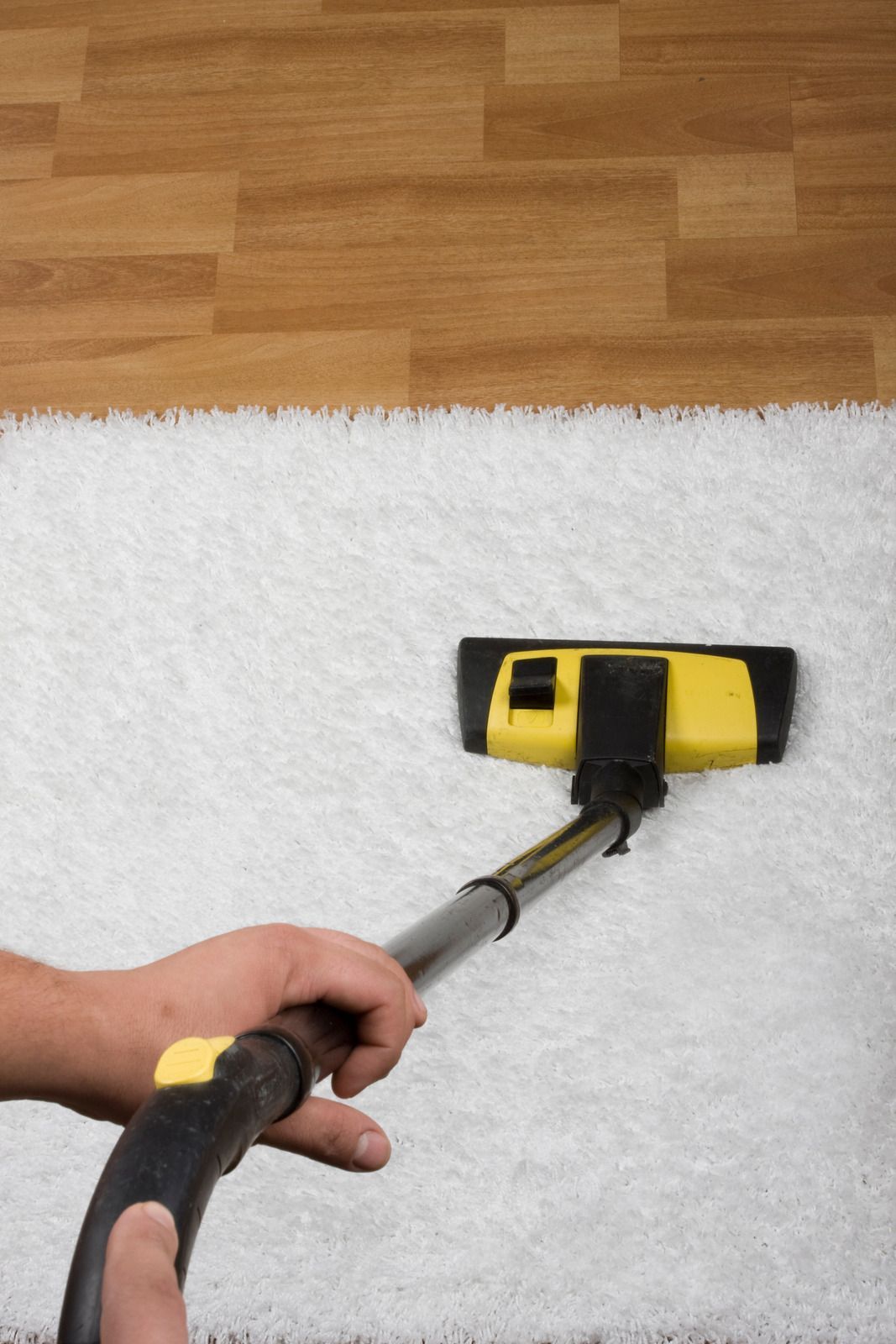 Person vacuuming a white fluffy rug; wooden floor in background. Black and yellow vacuum.