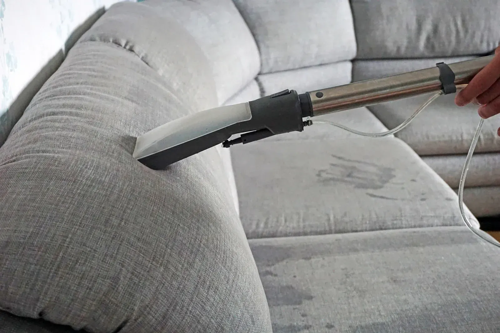 A person using a upholstery cleaner on a gray sectional couch.