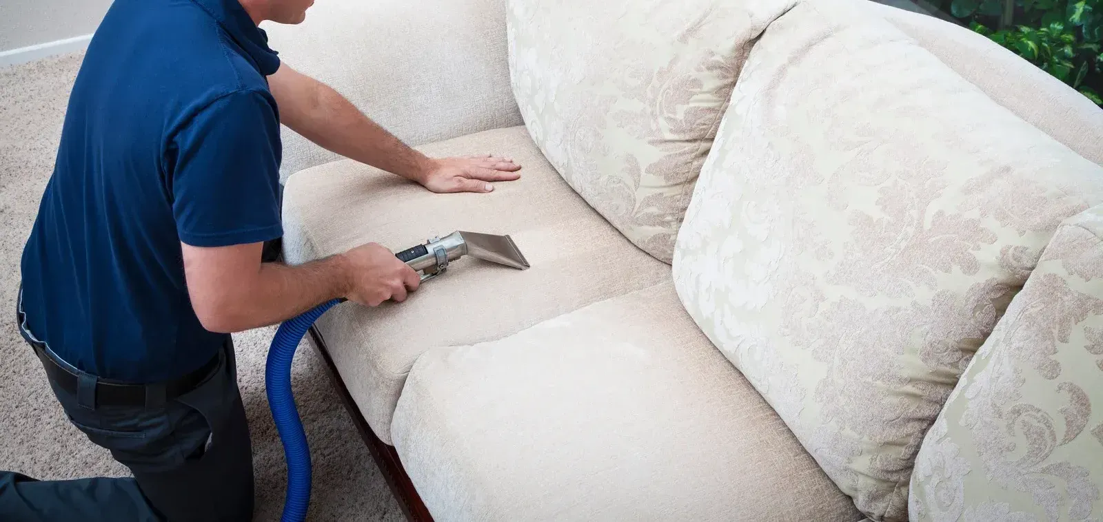 A man is cleaning a couch with a vacuum cleaner.