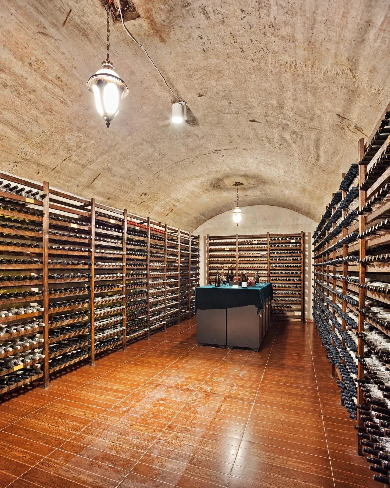 Wine cellar with rows of bottles on wooden shelves and a central tasting table under arched stone ceilings