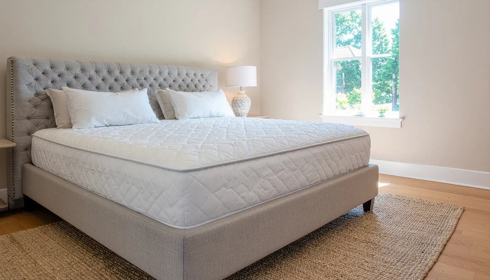 Bedroom with gray upholstered bed, tufted headboard, white bedding, and rug near a window.