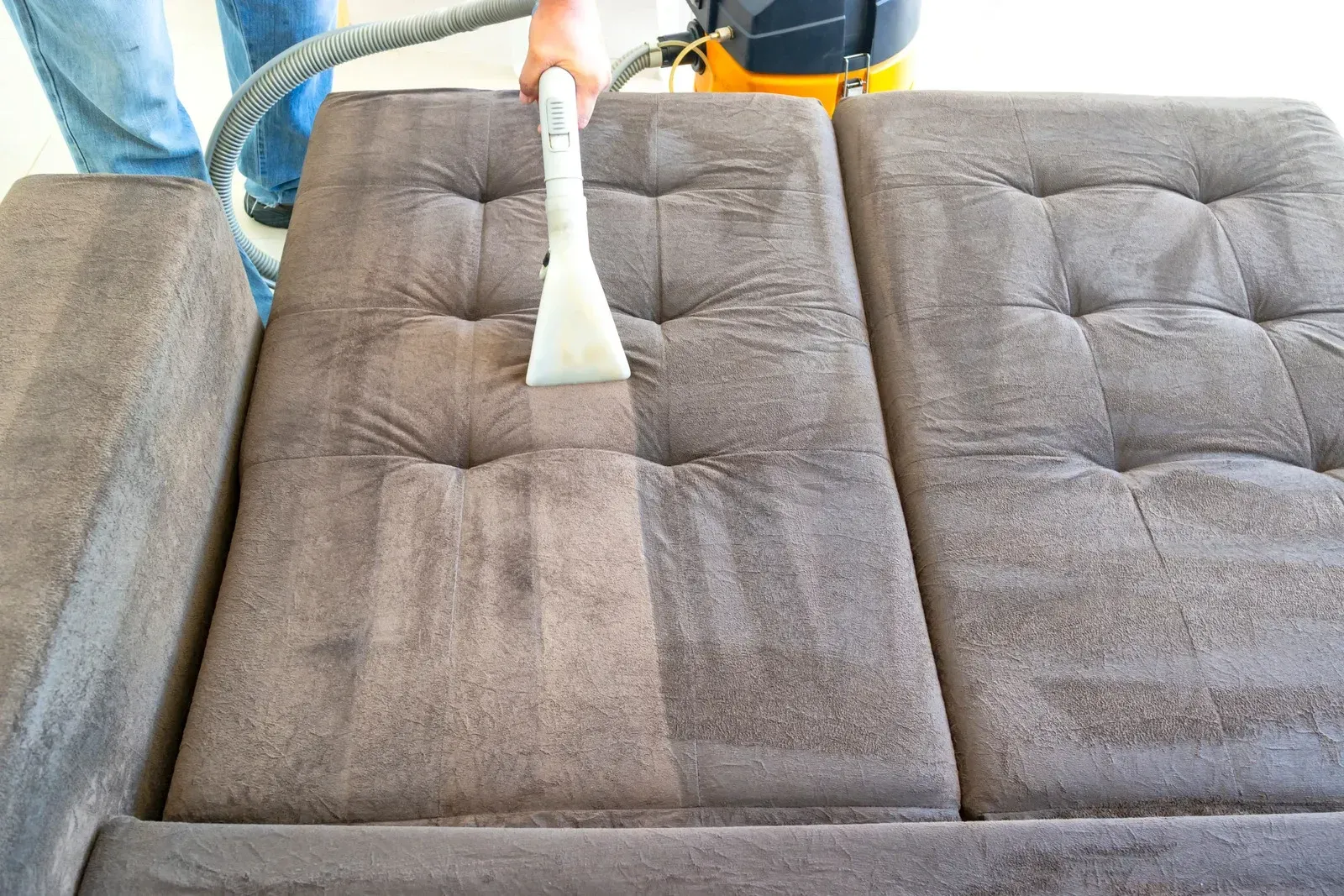 Person cleaning a brown sofa with a vacuum, revealing a cleaner surface.