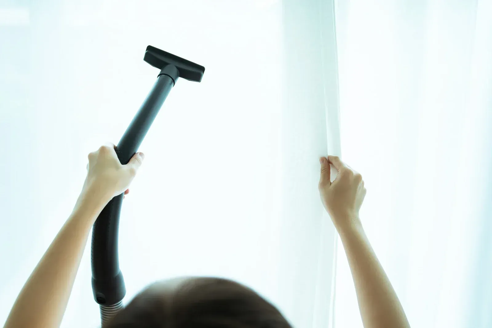 Person vacuuming white curtains.