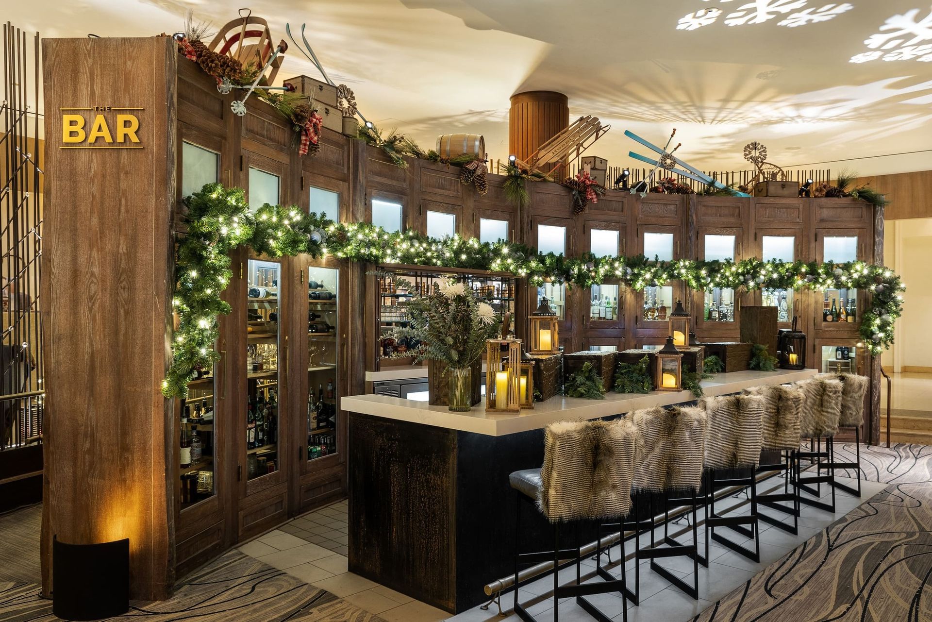 Stylish indoor bar with wooden decor, hanging plants, and high stools, warmly lit in a spacious venue