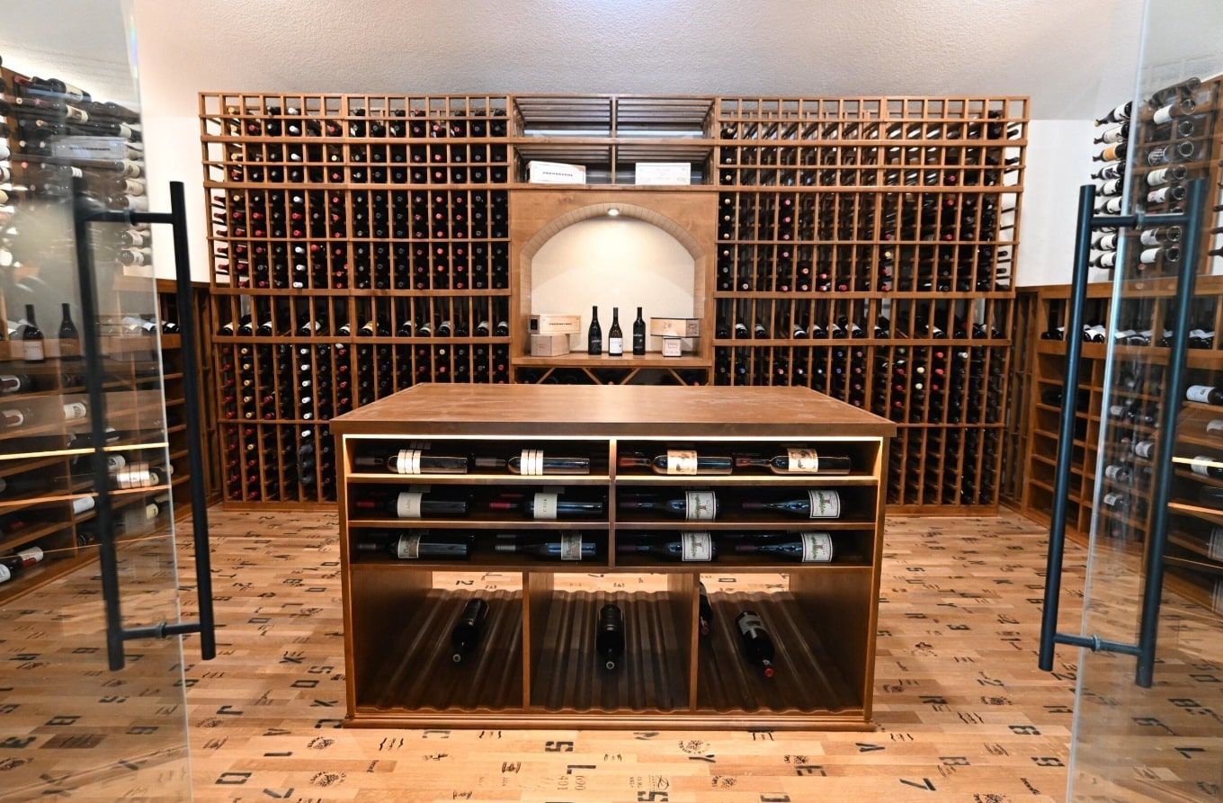 Wine cellar with wooden racks and shelves stocked with bottles, centered on a display cabinet in a warm-lit room