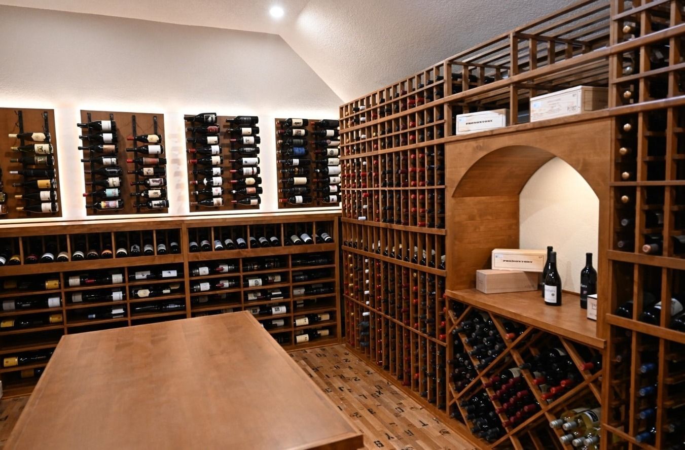 Wood-paneled wine cellar with built-in racks, a central tasting table, and an arched alcove with bottles and glasses