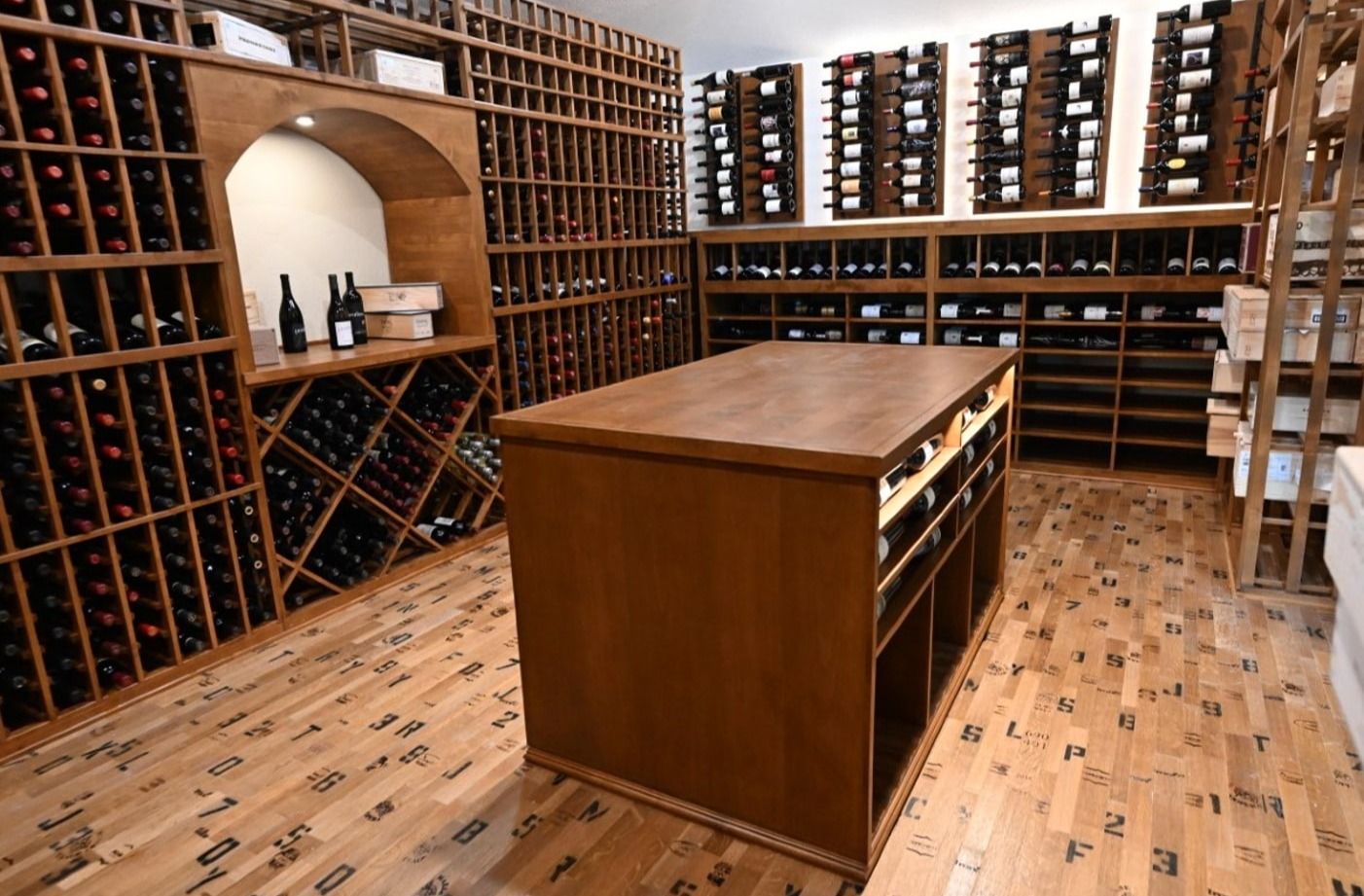 Wine cellar with wooden racks, bottles, and a central tasting table on a tiled floor