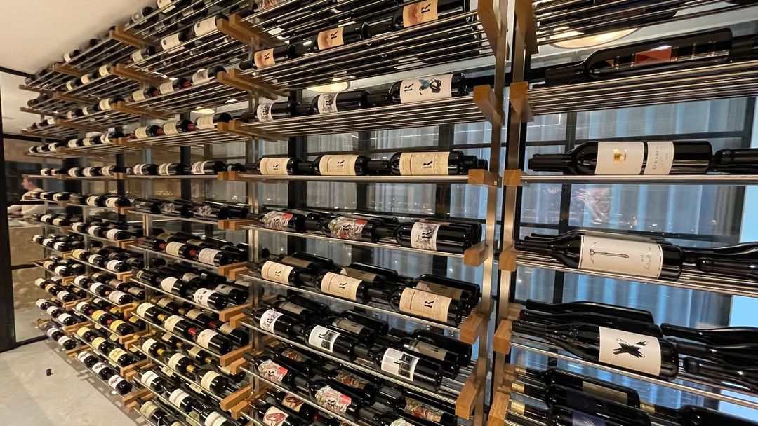 Rows of wine bottles stored horizontally on metal racks in a cellar or wine storage room.