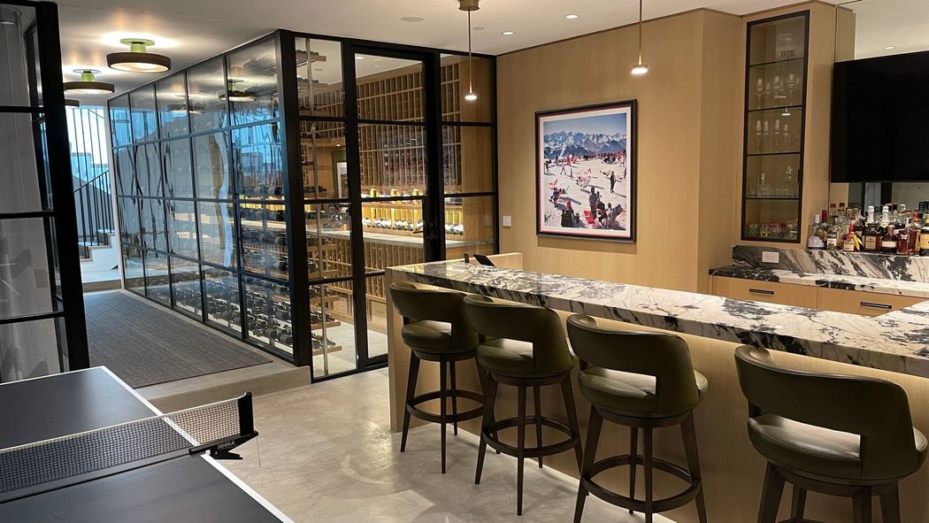 Modern bar interior with a marble counter, stools, glass shelving, and warm pendant lighting