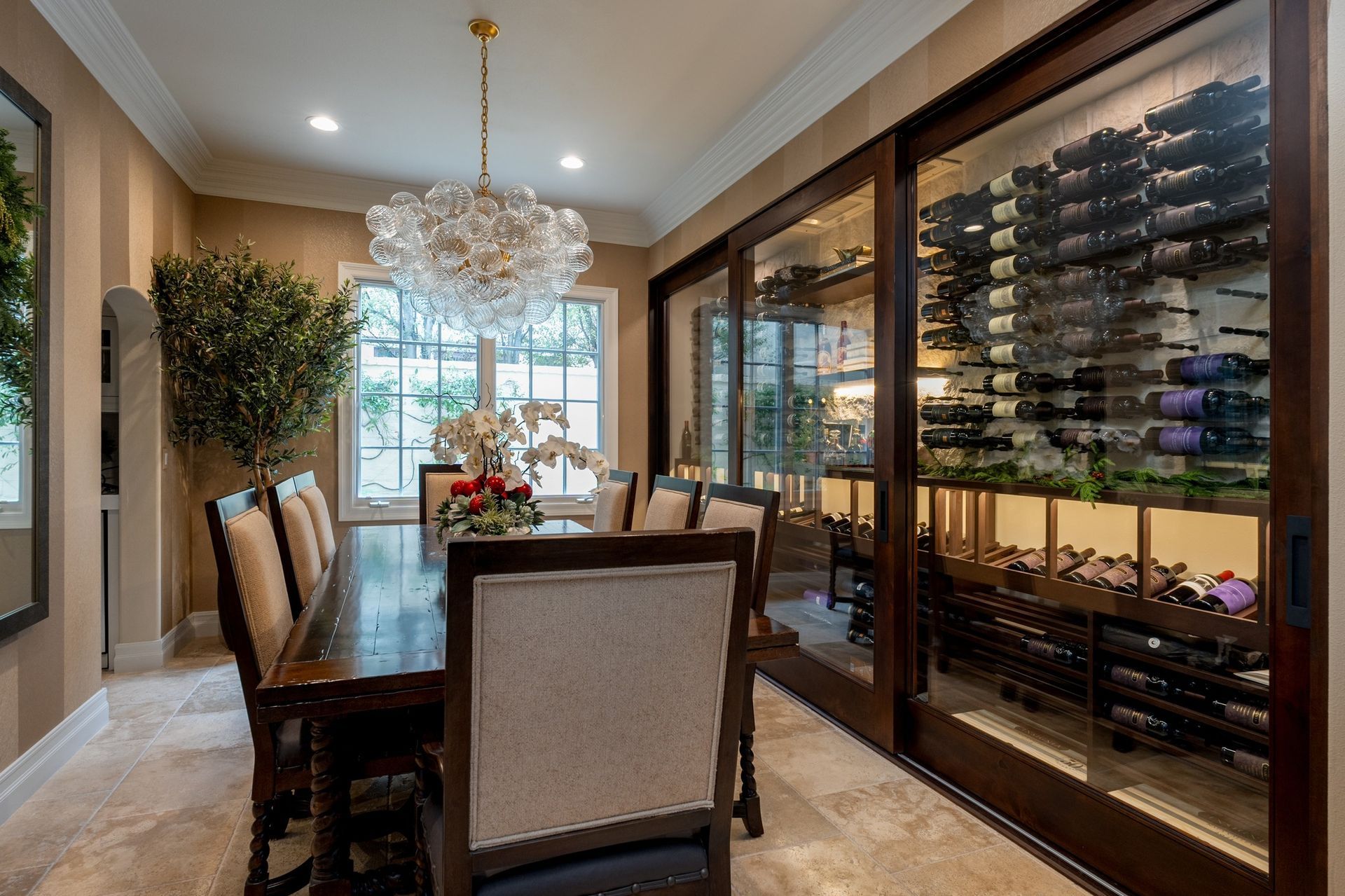 Elegant dining room with chandelier, glass wine display, and a dark wood table by bright windows
