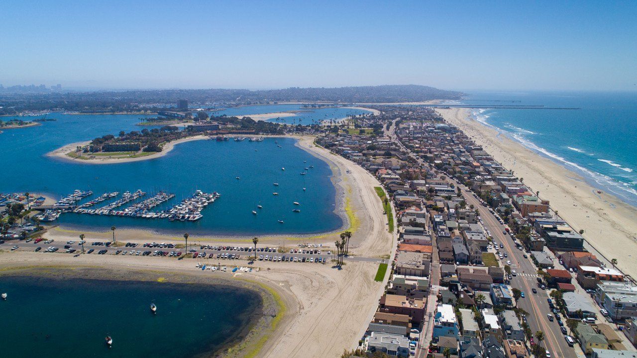 An aerial view of a beach with a harbor and a city in the background.