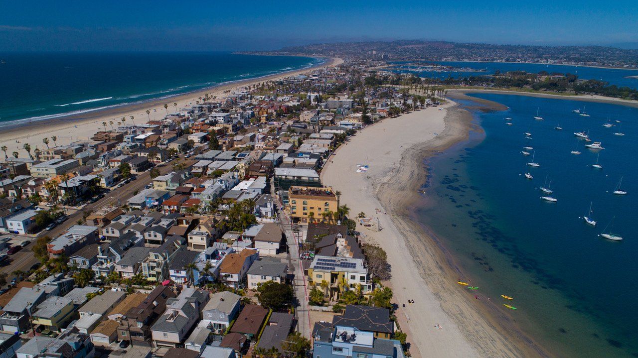 An aerial view of a beach with boats in the water and a city in the background.