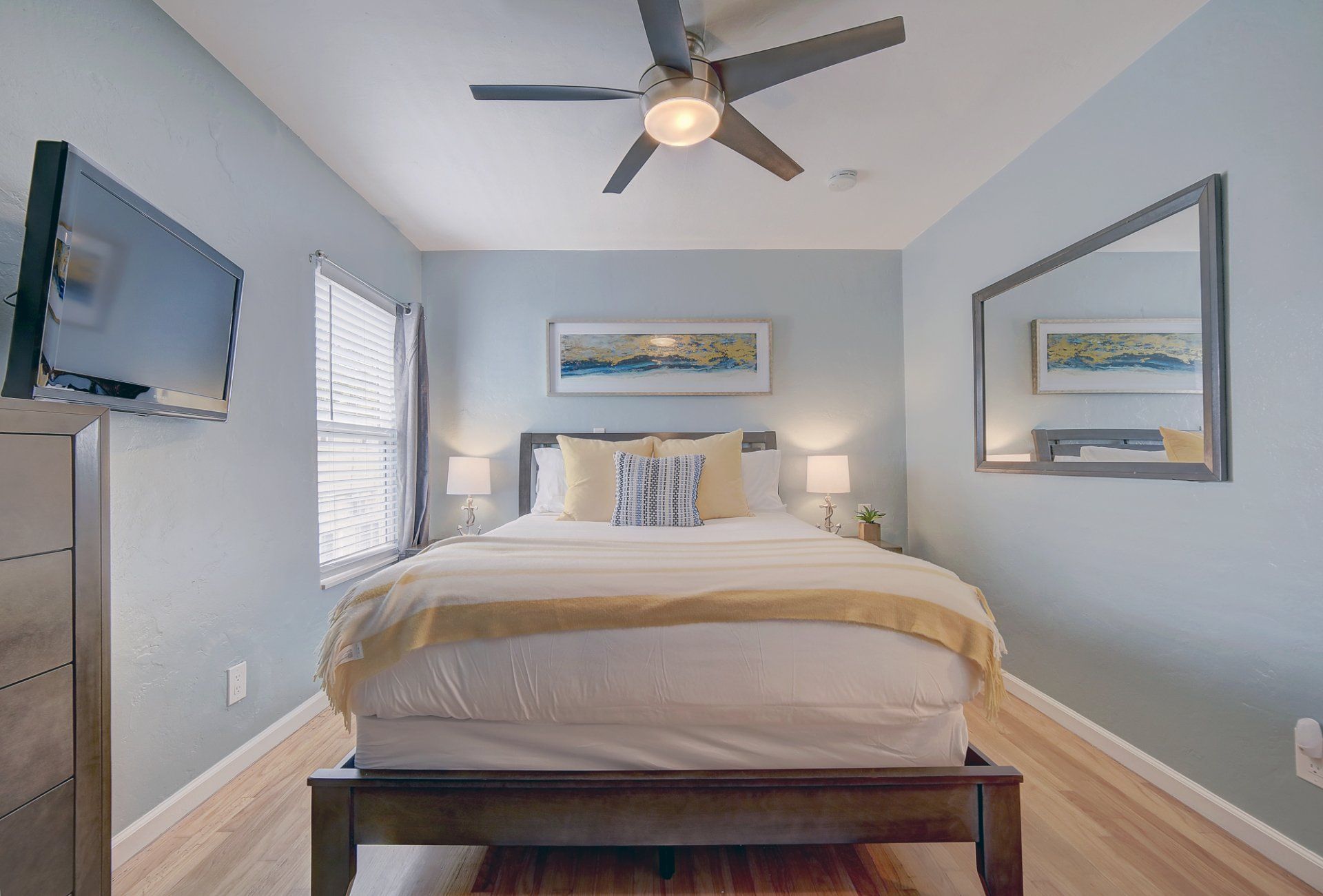 A bedroom with a bed , television , mirror and ceiling fan.