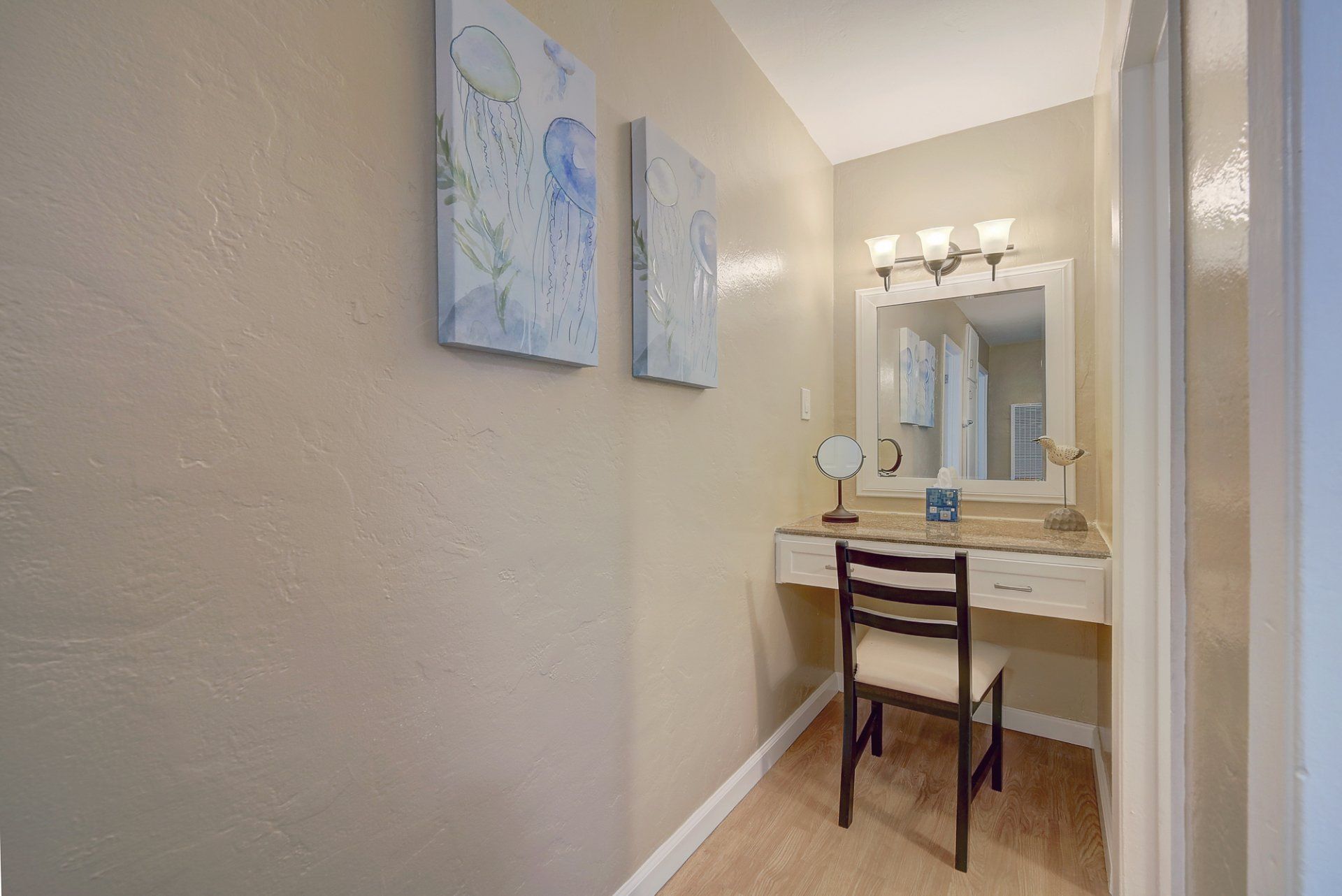 There is a vanity with a chair and a mirror in the hallway.