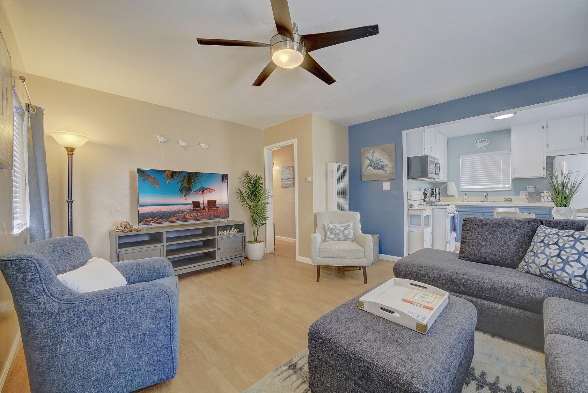 A living room with a couch , chairs , ottoman , television and ceiling fan.