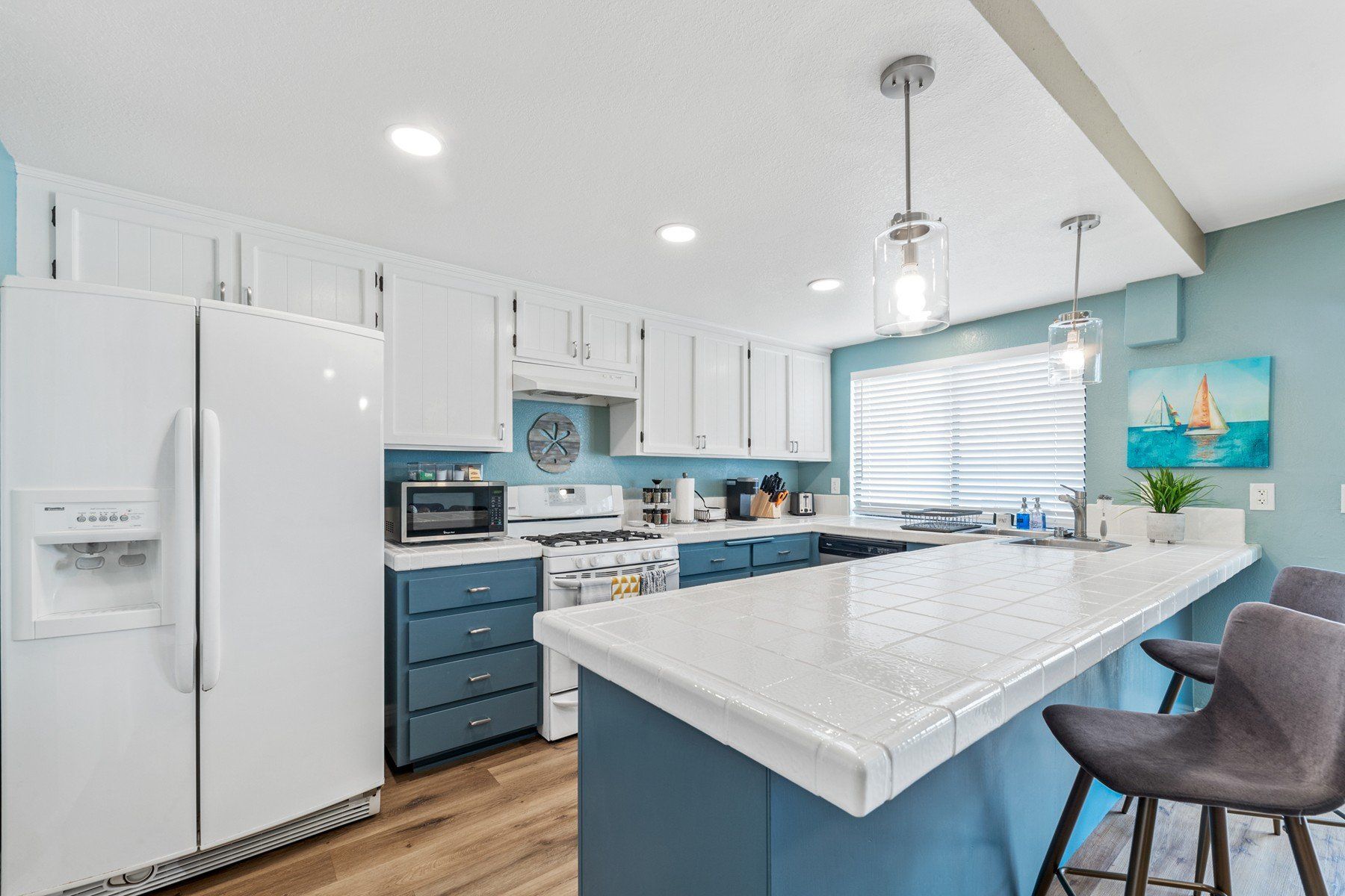 a kitchen with blue cabinets , a white refrigerator , a stove , a sink , and a bar .