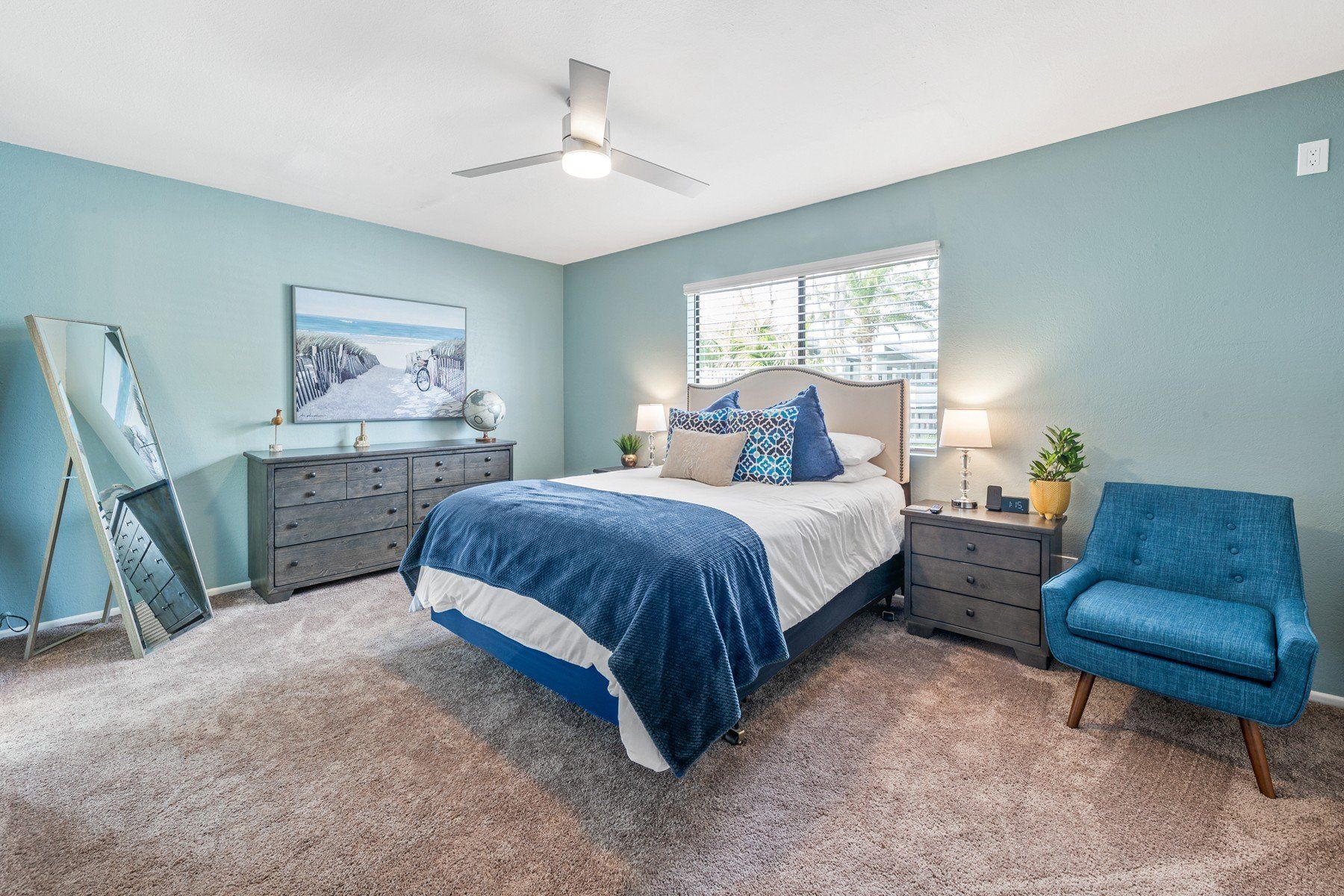 A bedroom with a bed , chair , dresser and ceiling fan.