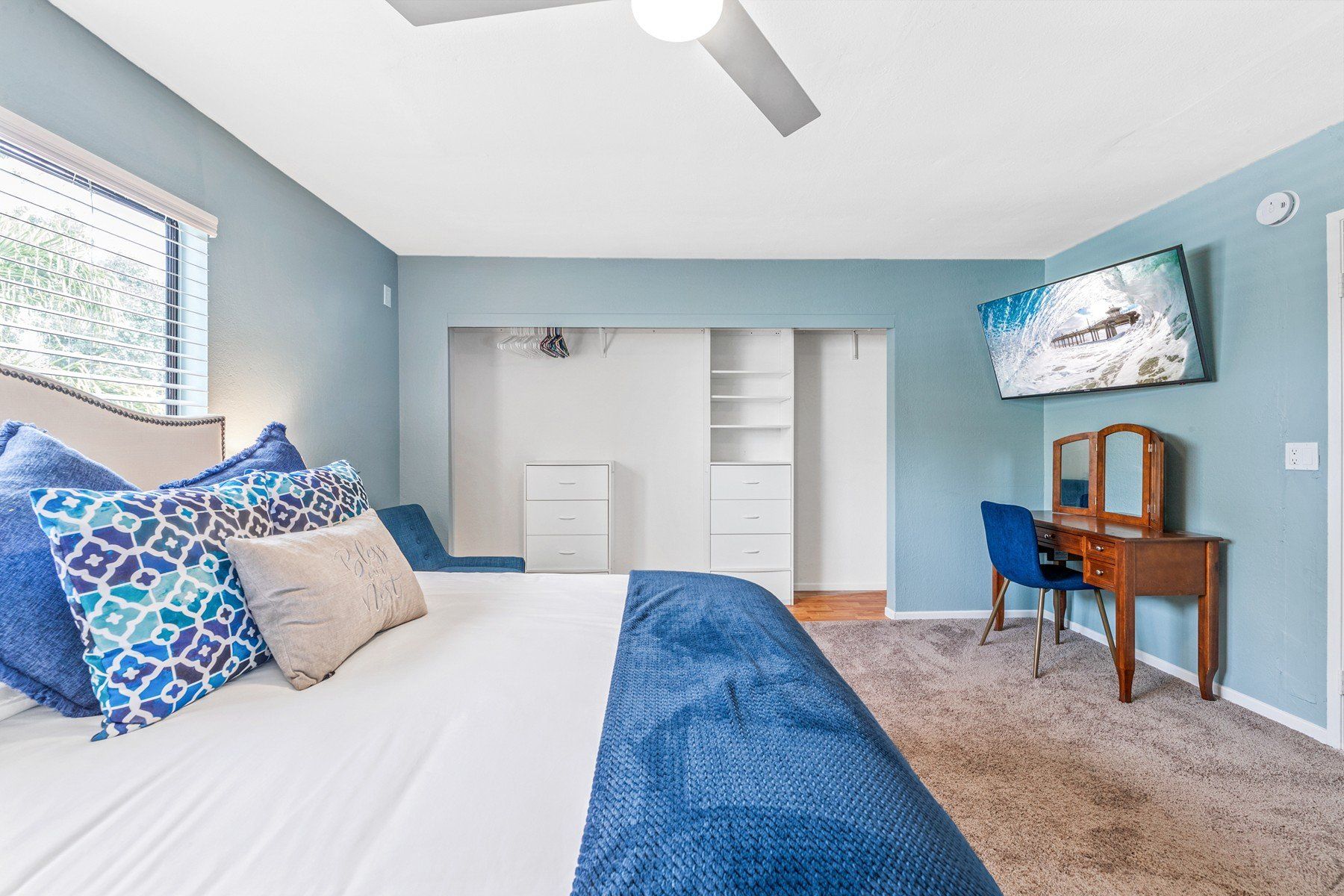 A bedroom with a king size bed , a desk , a television and a ceiling fan.