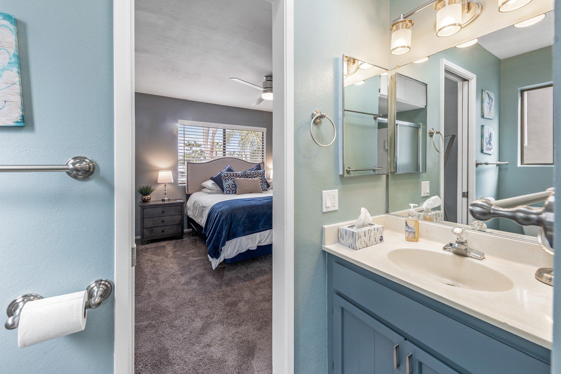 A bathroom with a sink and a mirror leading to a bedroom.