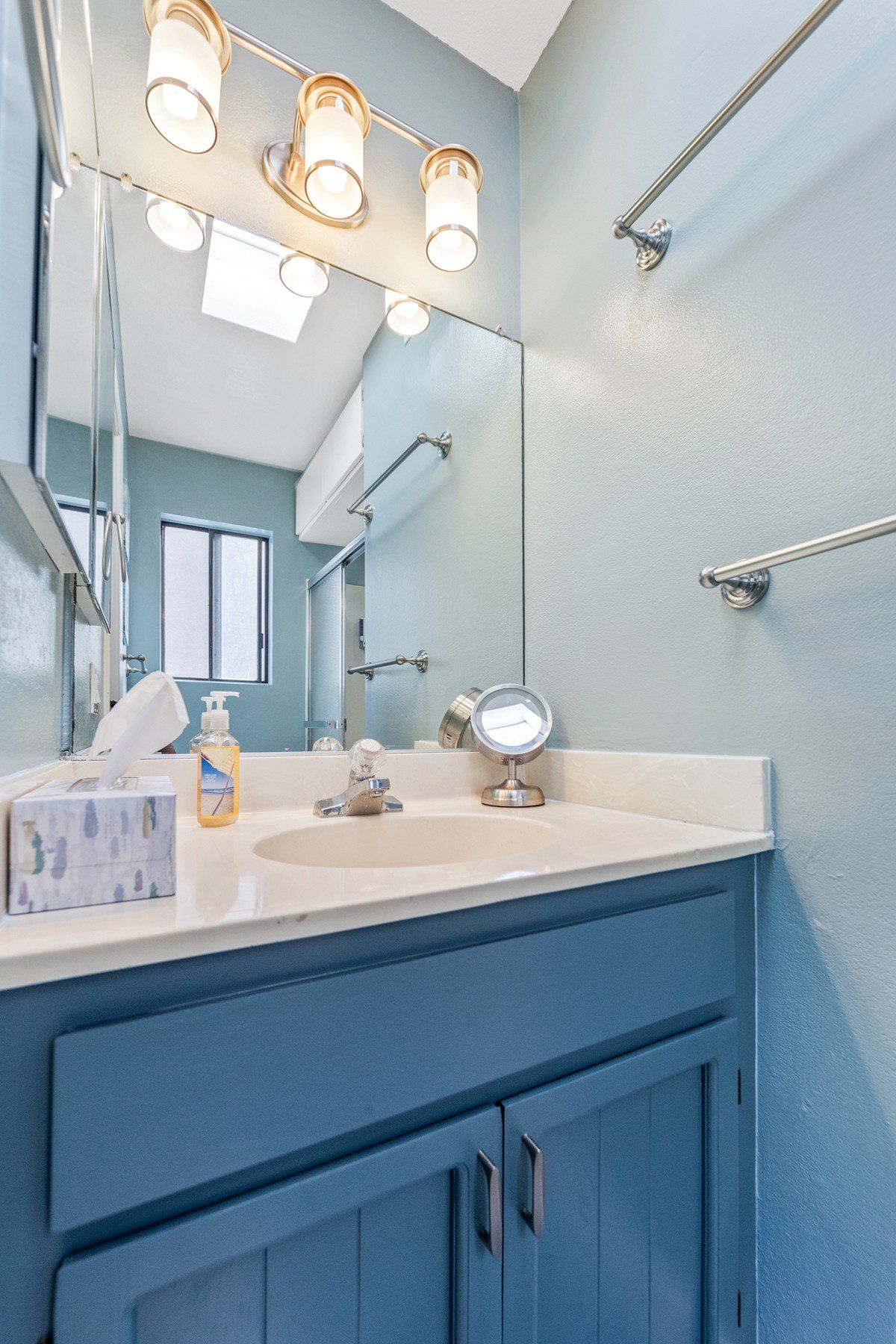 A bathroom with a blue vanity , sink , mirror and towel rack.