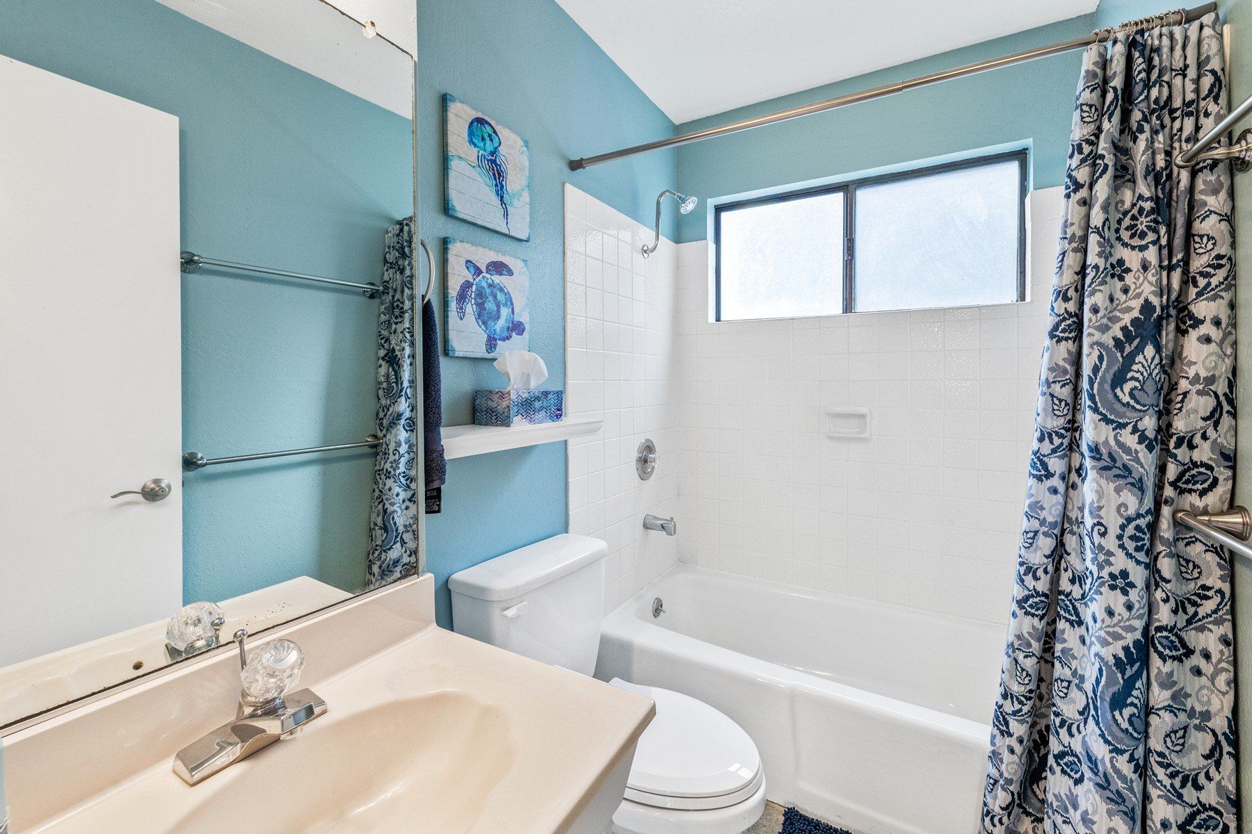 A bathroom with a toilet , sink , shower and window.