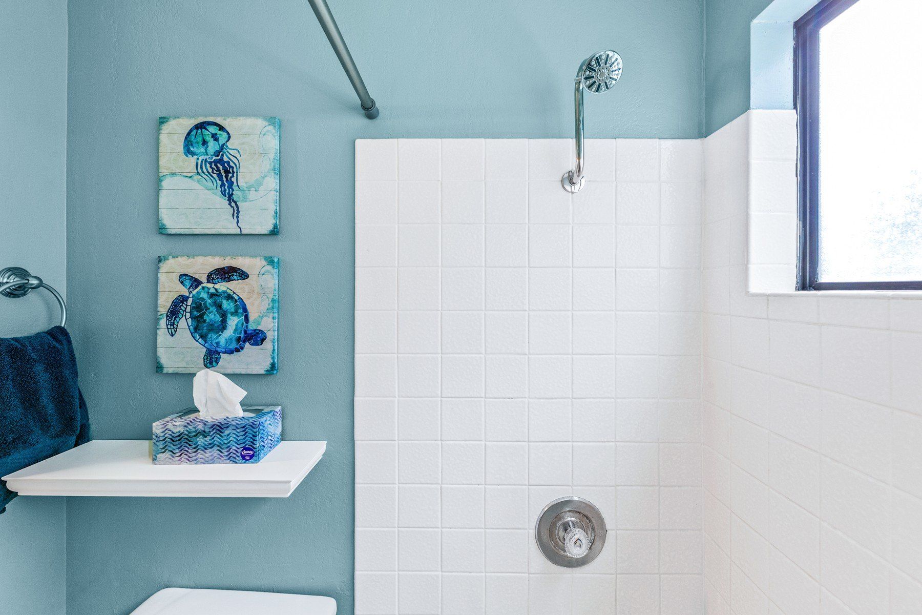 A bathroom with blue walls , white tiles , a toilet and a shower.