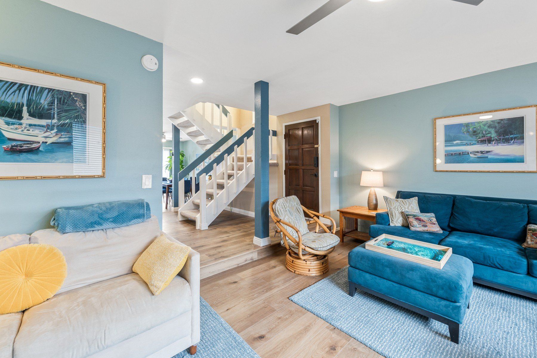 A living room with a blue couch , ottoman , chair and stairs.