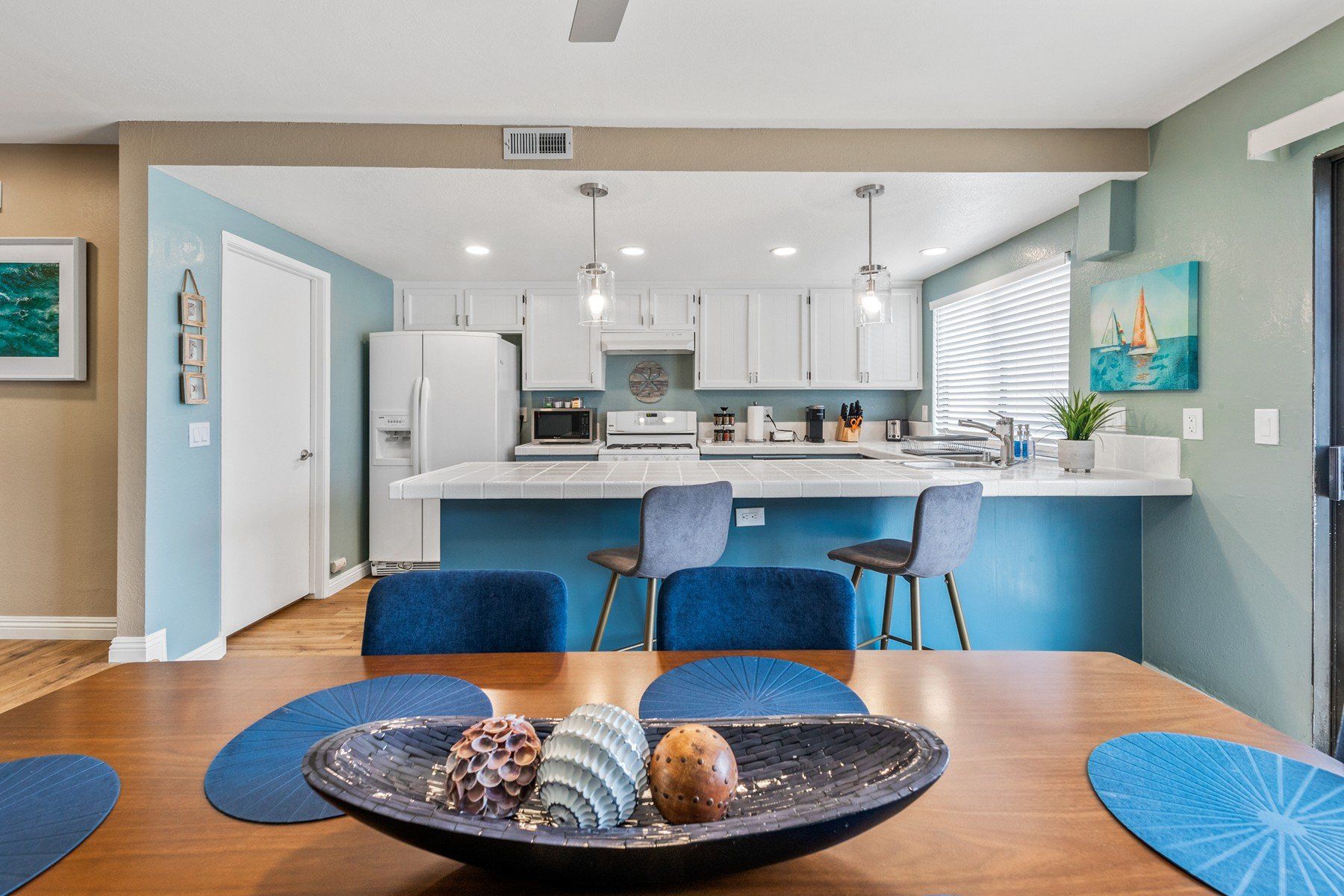 a dining room table with a bowl of seashells on it and a kitchen in the background .