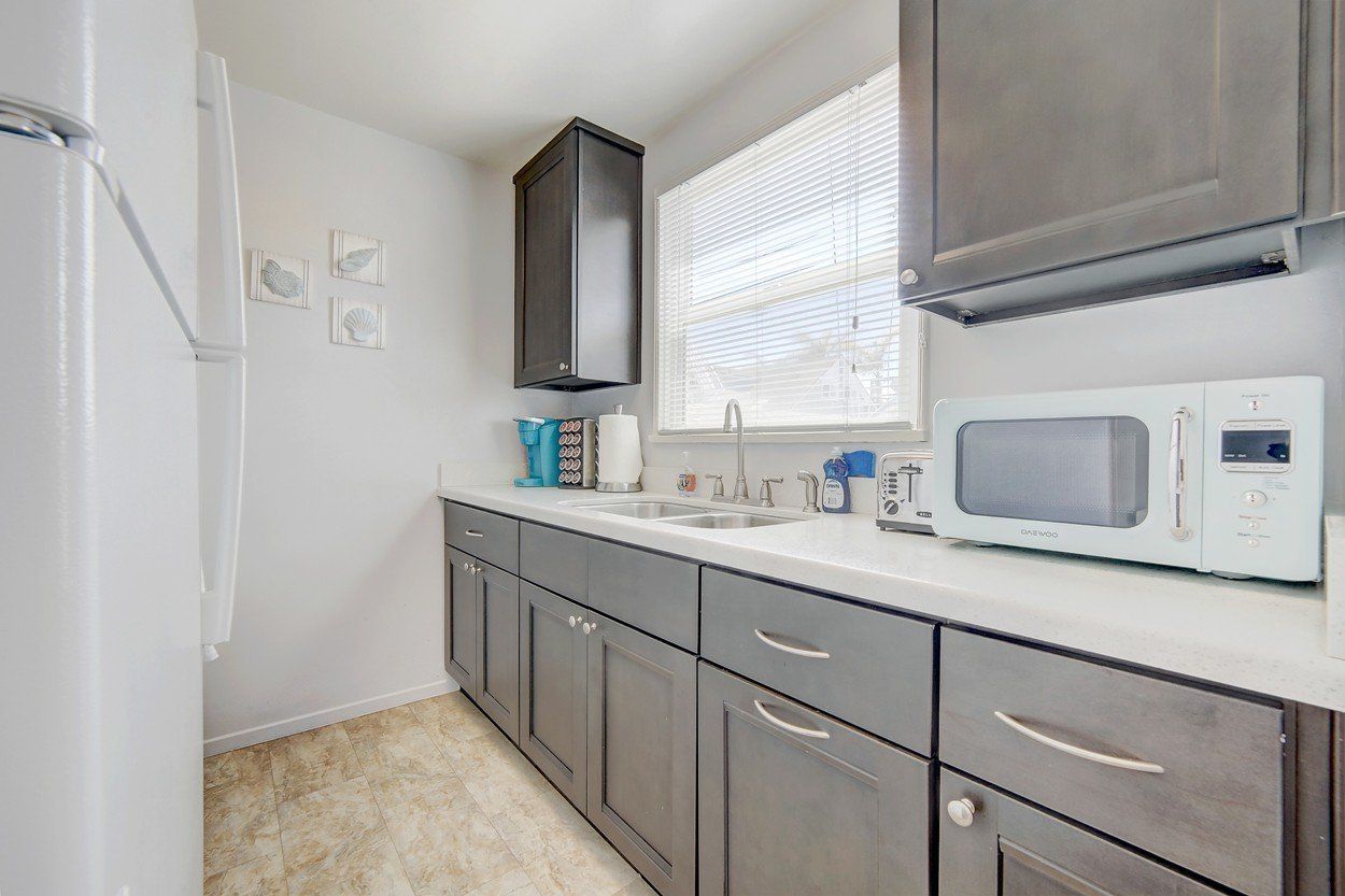 a kitchen with gray cabinets , a white refrigerator , a microwave , and a sink .