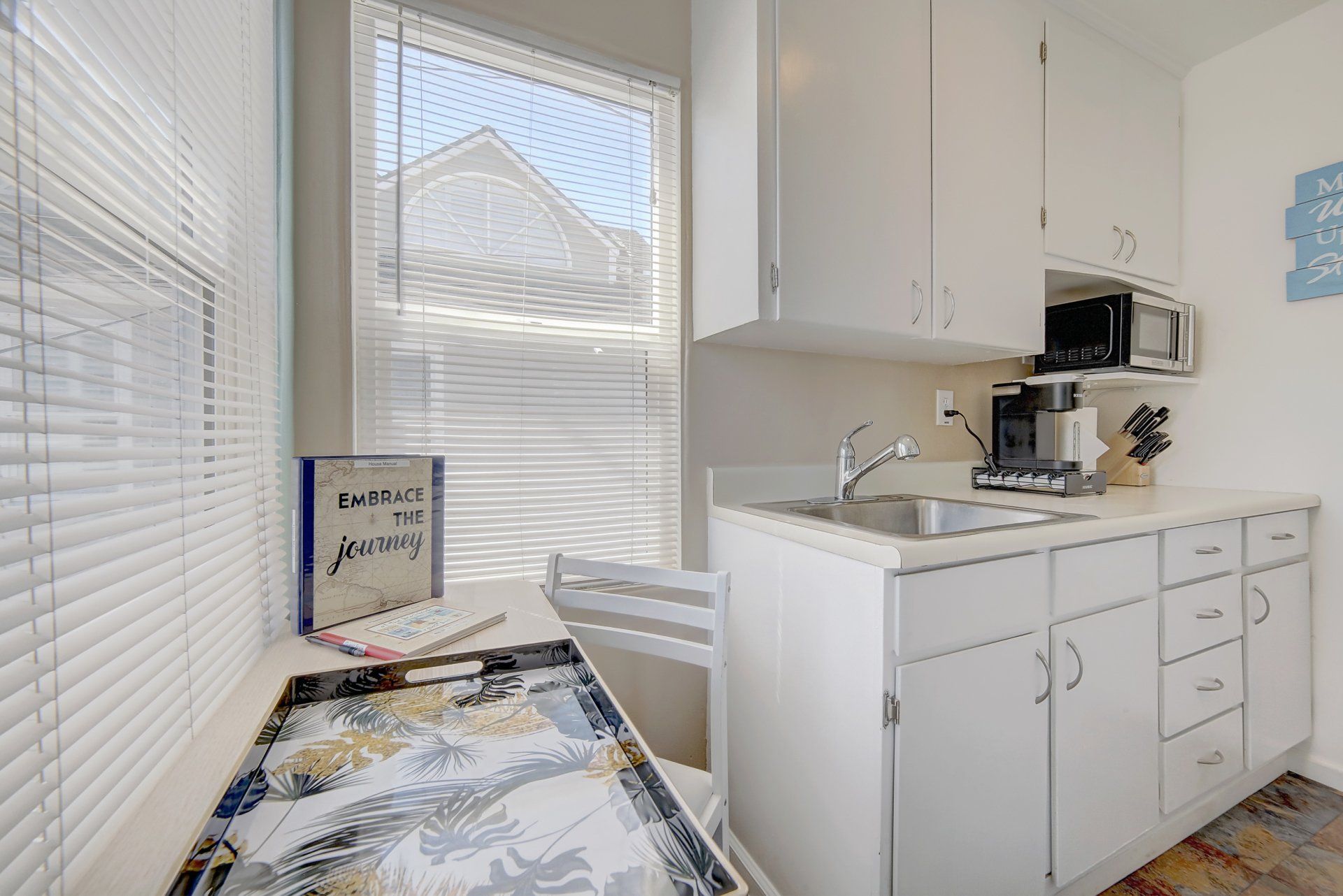 a kitchen with white cabinets , a sink , a microwave and a window .