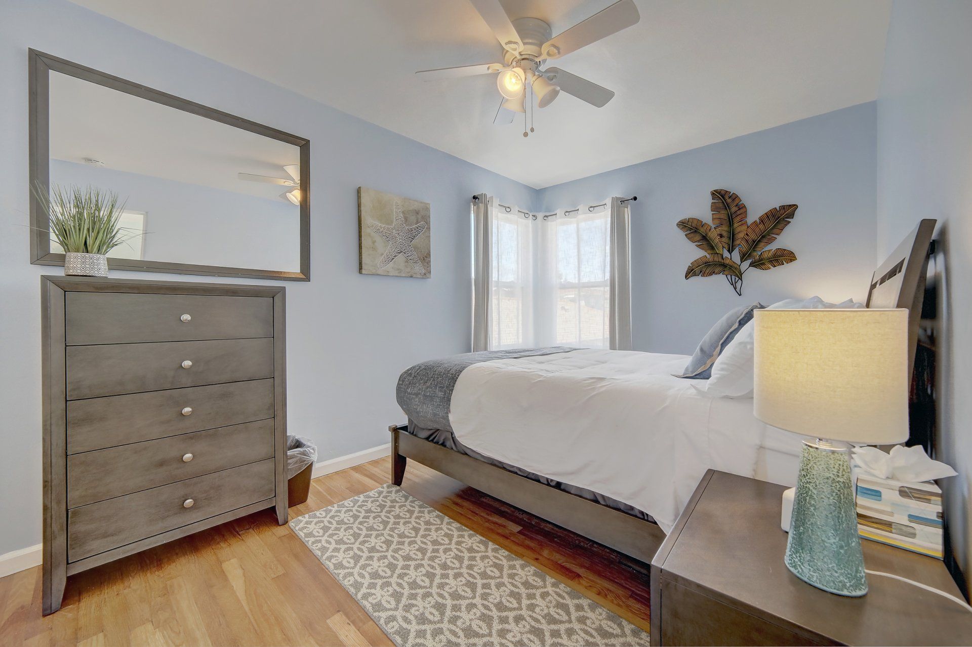 A bedroom with a bed , dresser , nightstand , mirror and ceiling fan.