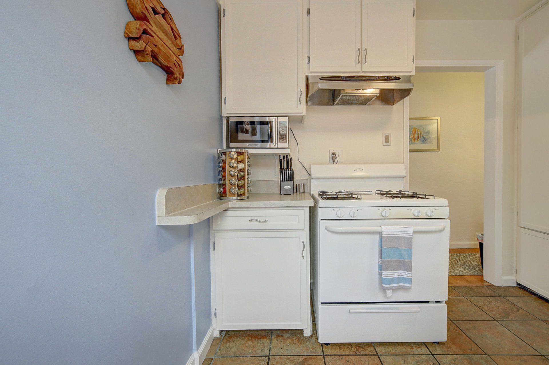 A kitchen with white cabinets , a stove and a microwave.