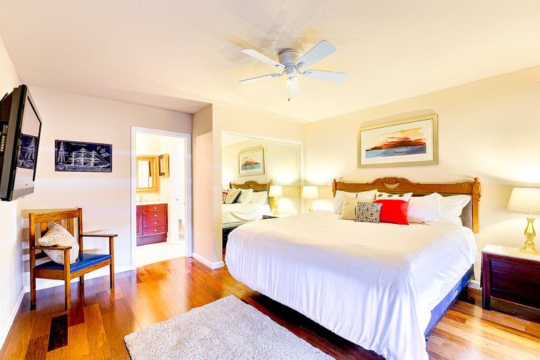 A bedroom with a king size bed , a chair , a television and a ceiling fan.