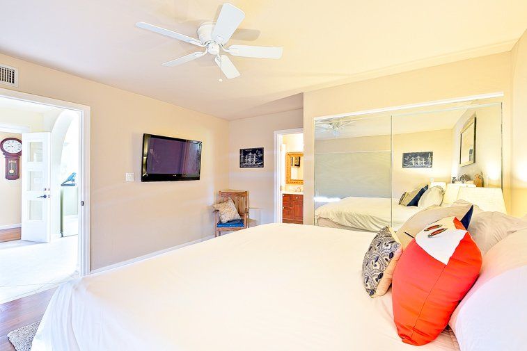 A bedroom with a large bed , ceiling fan , television and mirrored closet.