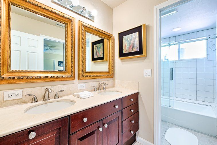 A bathroom with two sinks , two mirrors and a toilet.