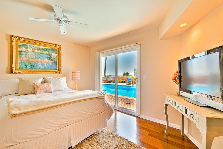 A bedroom with a large bed , television , and sliding glass doors leading to a pool.