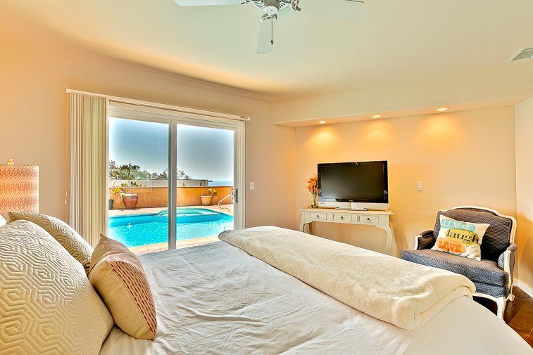 A bedroom with a king size bed , television , chair and sliding glass doors leading to a pool.