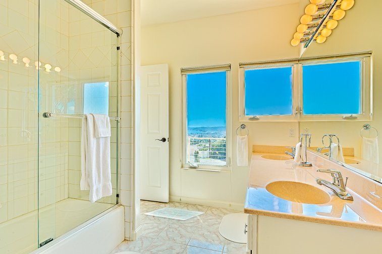 A bathroom with a sink , tub , mirror and two windows.