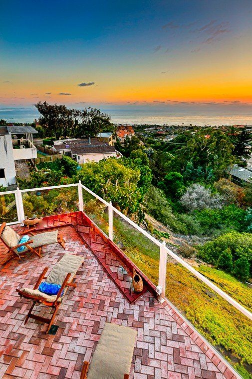 A balcony with chairs and a view of the ocean at sunset.